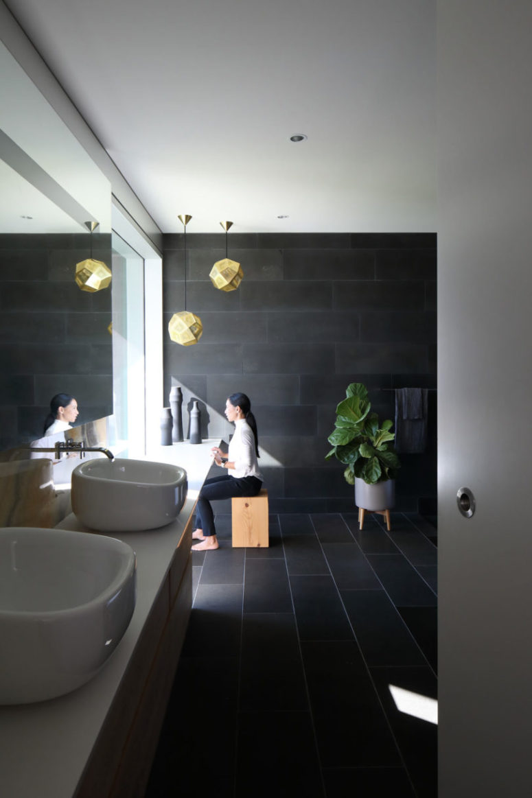 The bathroom is clad with dark tiles, sculptural sinks and some wooden touches for a spa feel