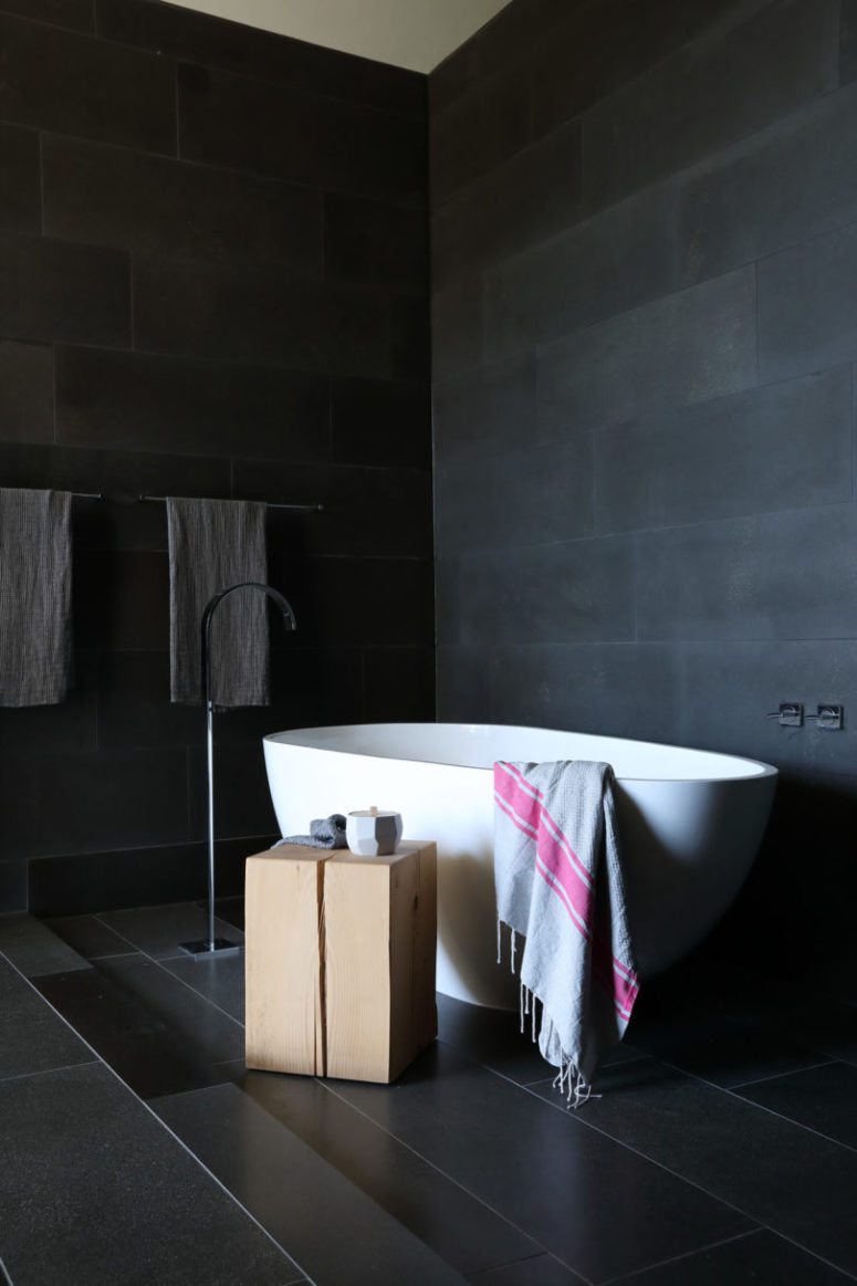 The bathtub is sculptural and a wooden slab side table contrasts with it