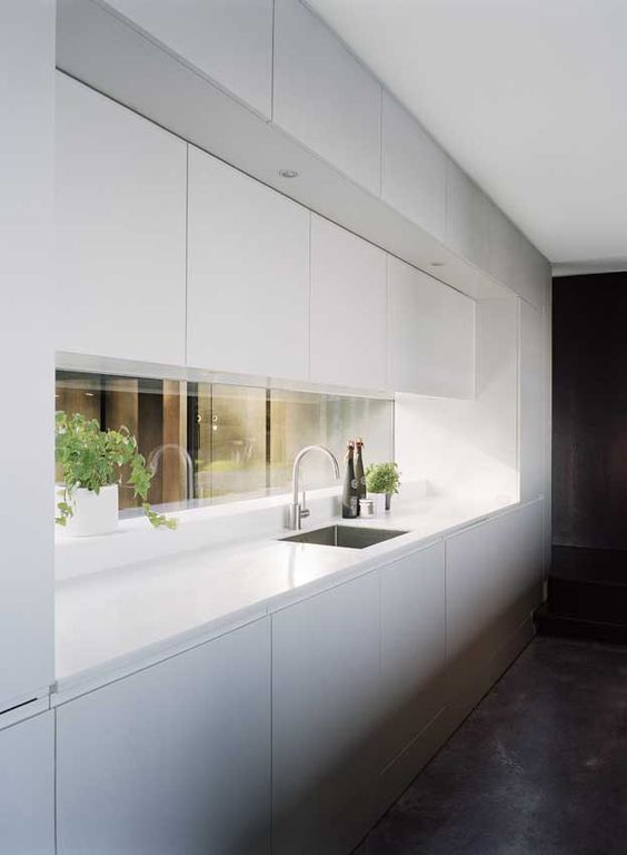 a minimalist kitchen in white with a window backsplash to give a touch of color and more interest to the space