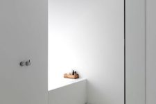 10 an ultra-minimalist bathroom in white with a glass shower and a wooden stool