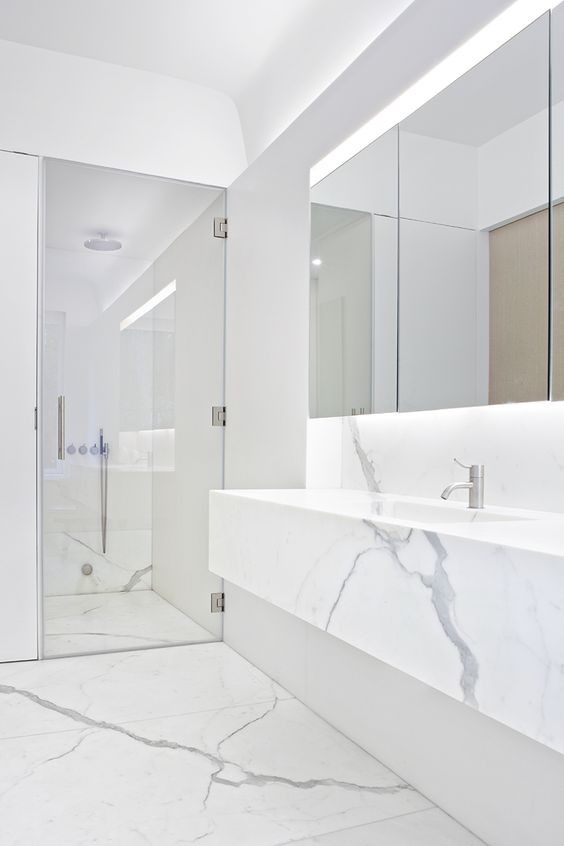 a minimalist white marble bathroom with a large mirror, a shower and a marble vanity