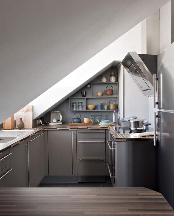 a small attic industrial kitchen with grey cabinets and stainless steel with a large skylight