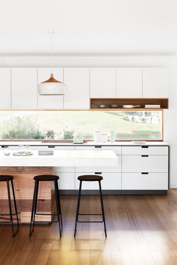 a minimalist white kitchen with a window backsplash that brings light in and lets enjoy the views