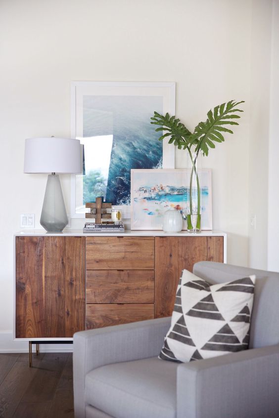 a modern console with a couple of oceanside artworks and tropical leaves in a vase