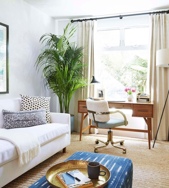 A modern boho space with a convertible sofa and a mid century wooden desk by the window