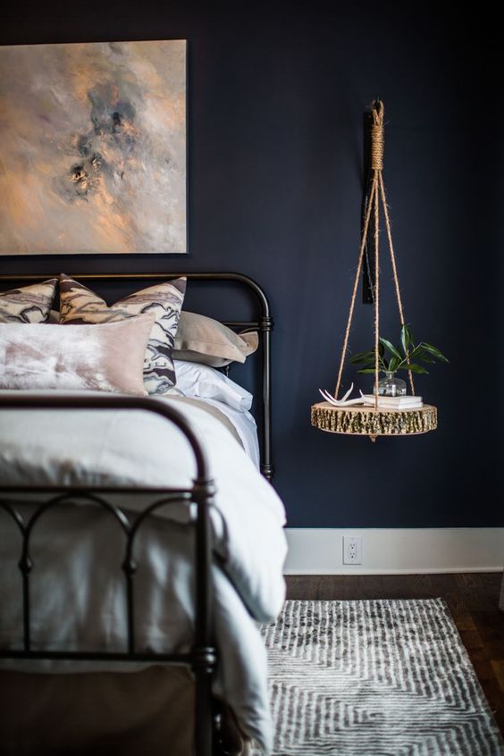 a moody bedroom with a hanging bedside table of a raw edge wood slice and twine for a rustic touch