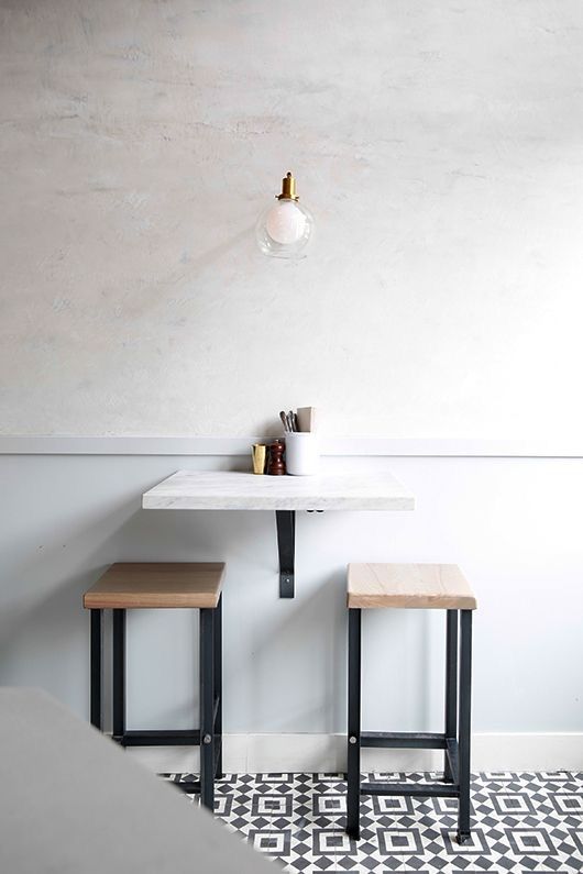 A small breakfast space with a wall mounted table and a couple of matching stools plus a lamp over it