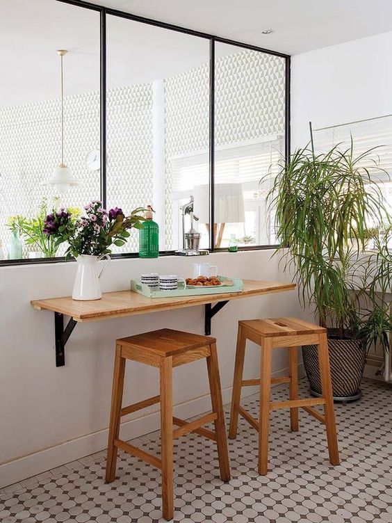 A small breakfast space with a wall mounted tabletop, wooden stools and some greenery around it