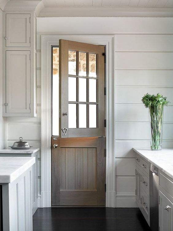 a stained wood Dutch door adds a rustic feel to the all-white kitchen with paneling
