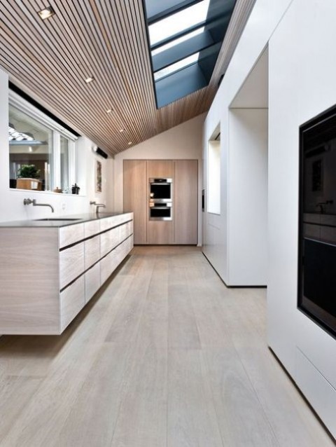 a minimalist kitchen done with wood and with several skylights plus additional lights to make the space cmfier