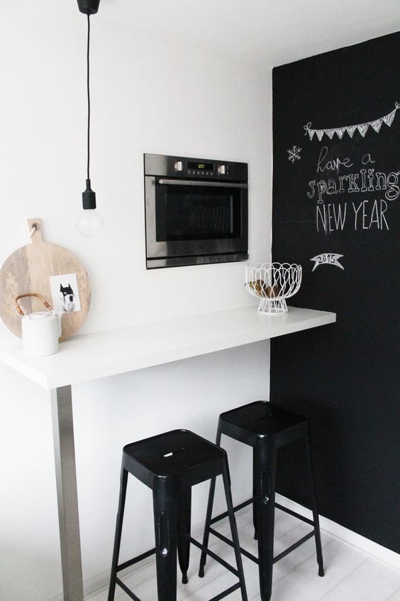 a tiny breakfast nook with a wall-mounted table, black stools and a chalkboard wall