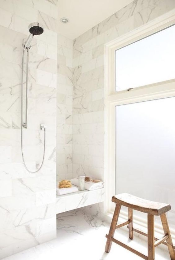 white marble tiles, frosted glass windows and a wooden stoll create a welcoming bathing space