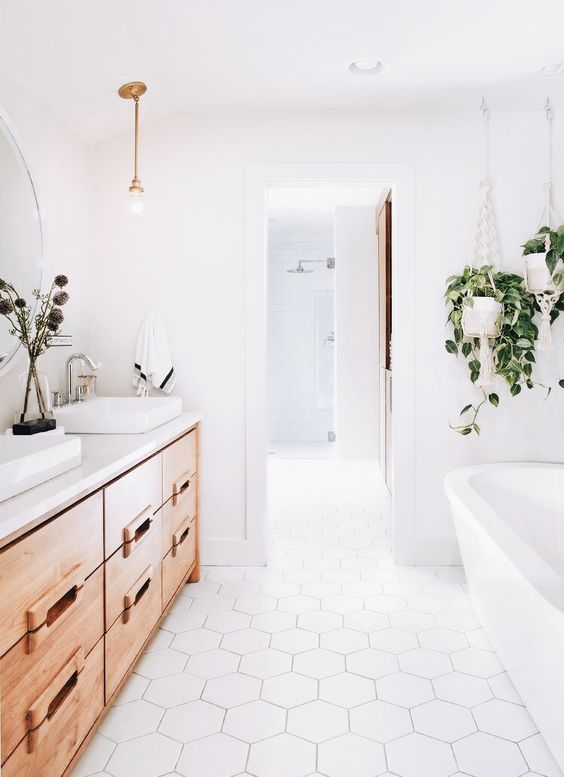 a clean white space with a large light-colored wood vanity and some potted greenery