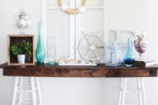 21 a console table with colored bottles, greenery, a lantern and some shells in jars for a seaside feel