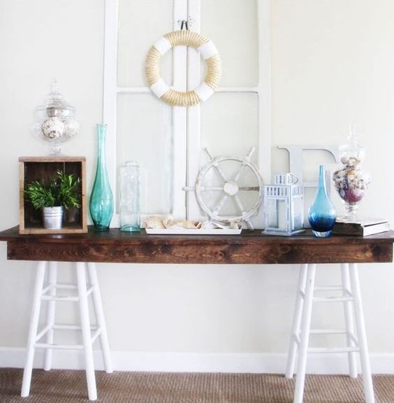 a console table with colored bottles, greenery, a lantern and some shells in jars for a seaside feel