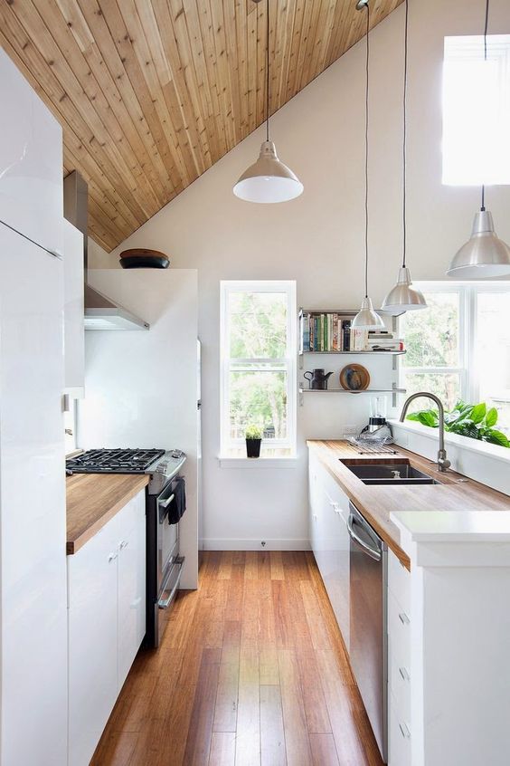 a double height narrow kitchen with many windows that flood the space with light, and wooden touches for coziness