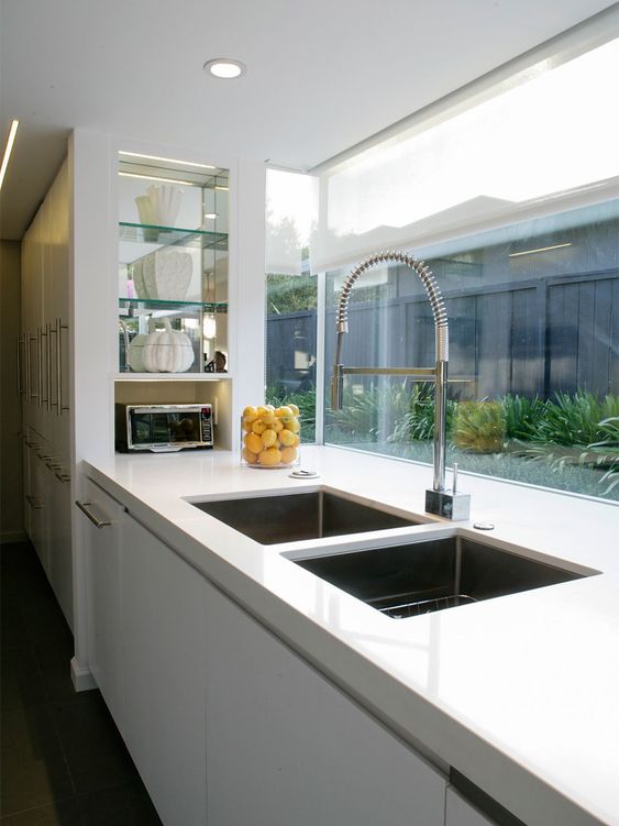 a glossy white kitchen is connected to the private courtyard through a large window