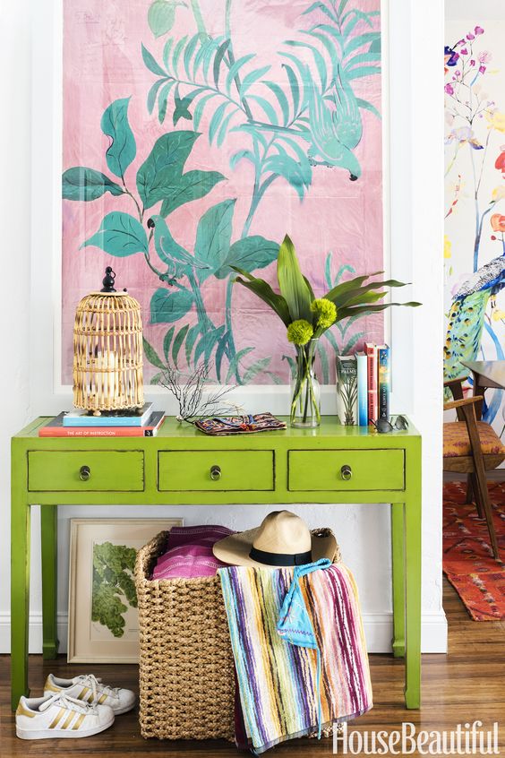 a super colorful console with a birdcage candle holder, greenery, a bold artwork and a basket with colorful textiles