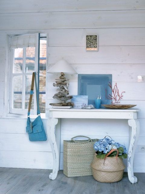 a small console with corals, a driftwood lamp, an abstract artwork and baskets under the table