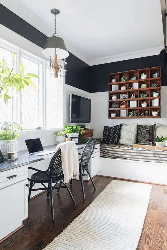 A black and white guest bedroom with white shiplap walls, a double desk and black chairs, a built in bed, a TV and a stained shelving unit