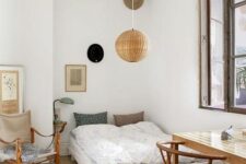 a cool guest bedroom with a low bed and printed bedding, a stained desk and woven chairs, a pendant lamp and some decor