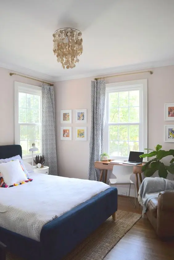 a pretty pink guest bedroom with a navy bed and neutral bedding, a stained desk and a white chair,a  leather chair and some artwork
