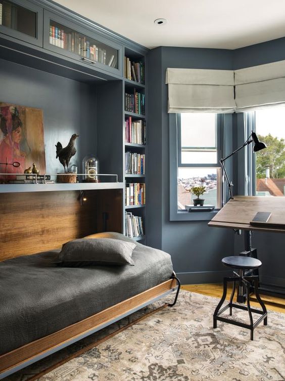 A vintage slate blue guest bedroom with built in bookcases and a Murphy's bed, a desk and a stool