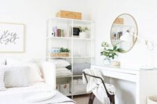 a white guest bedroom with a bed with storage drawers, a white desk and a metal chair, a storage unit and a round mirror