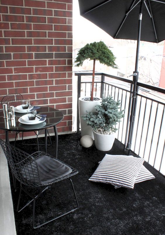 a black rug, a metal dining set, potted plants and a large umbrella for privacy and to protect from the sun