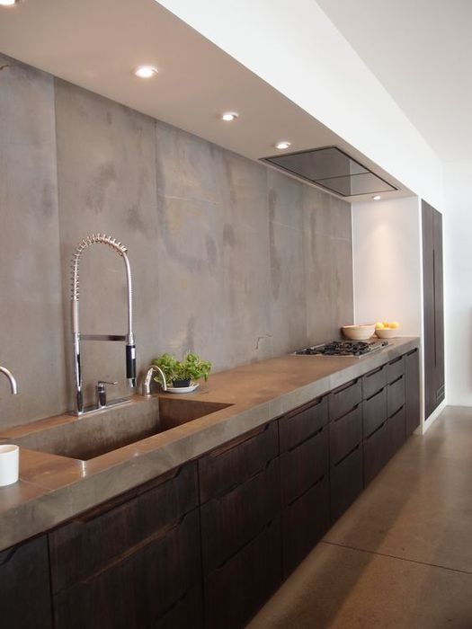 an industrial kitchen with dark metal cabinets and a concrete countertop plus a backsplash