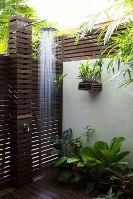 a gorgeous outdoor shower clad with dark stained wood and lots of potted plants plus a rain shower