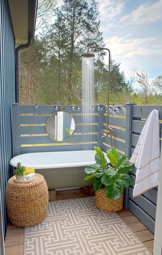 an outdoor bathtub plus a shower, wicker planters and a table and powder blue wooden planks all around for privacy