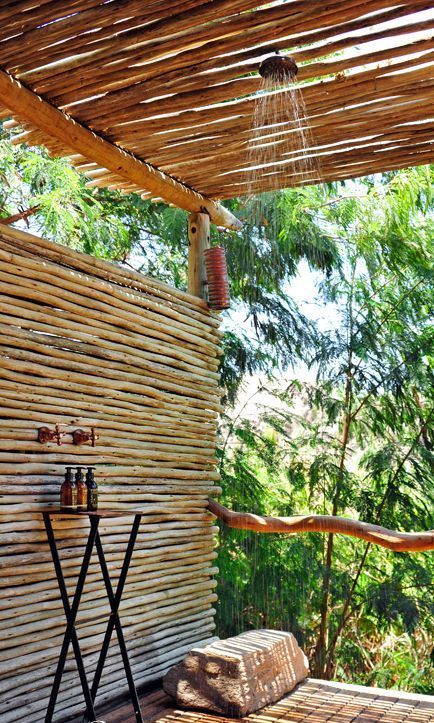 a wooden deck and walls and a roof made of wood sticks, a rain shower plus a small table with shampoos