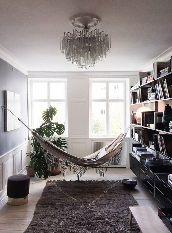a gorgeous reading nook with a hammock, a rug, ottomans and a bookshelf that separates the nook from the rest of the space