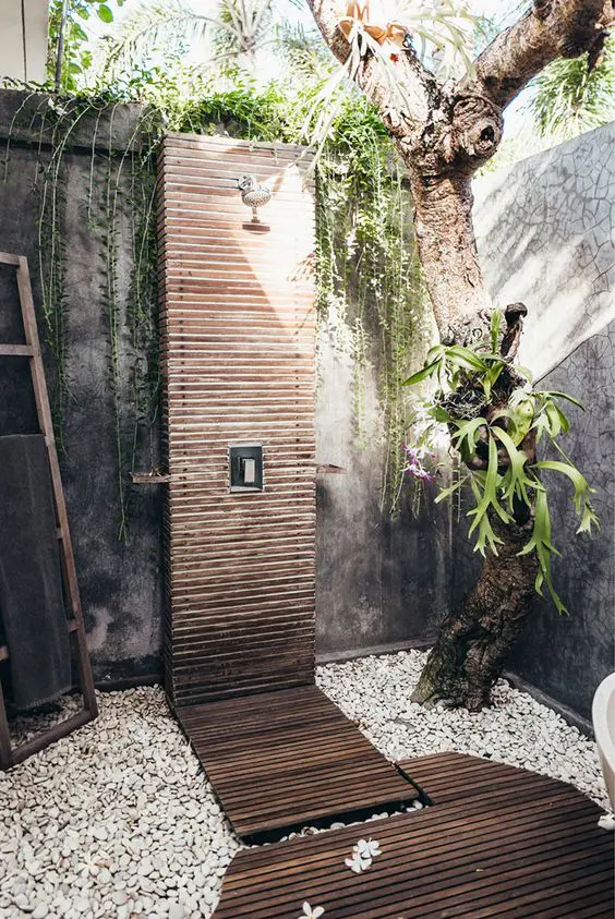 A spa like outdoor shower with pebbles, living plants and a tree and a wooden clad shower and a deck
