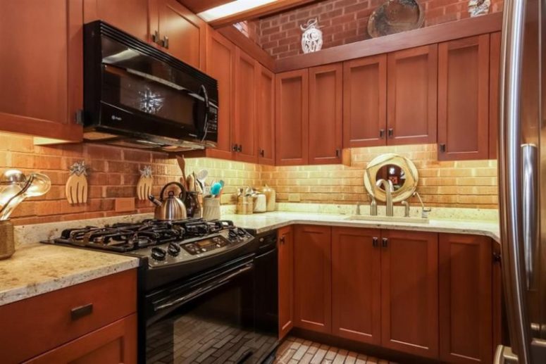 Red wood cabinets with marble countertops create a contrasting look and a brick backsplash adds to the space