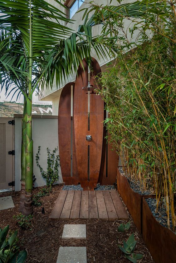 an outdoor shower space with a small wooden deck and metal surfboards plus palms around it