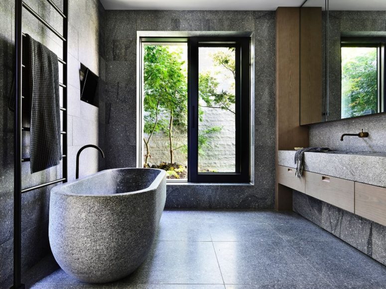 The bathroom resembles a natural spa with a larrge window, stone-like tiles and a real stone bathtub