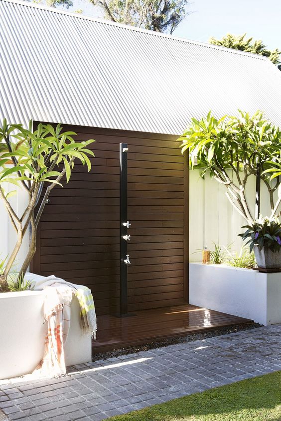 an outdoor contemporary shower with a dark stained wooden platform, potted trees around