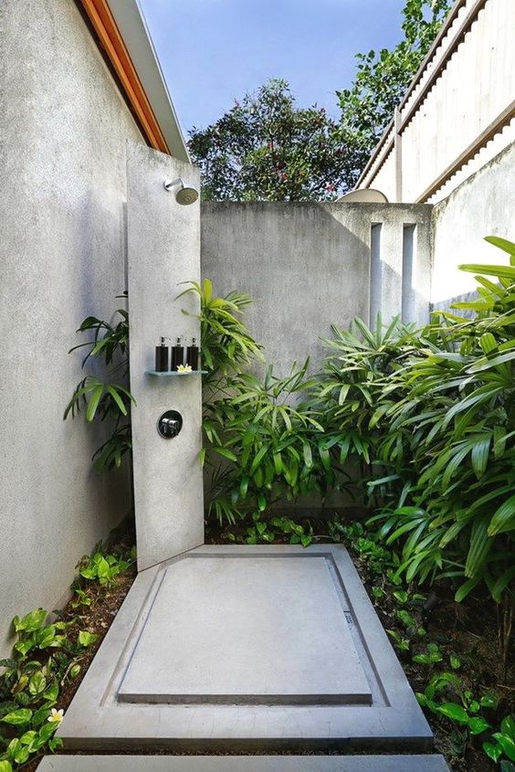 an outdoor shower space with a concrete shower spot and a panel plus lots of greenery around