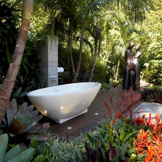 a backyard deck with some statues, a tile clad panel and an oval tub on a geometric base