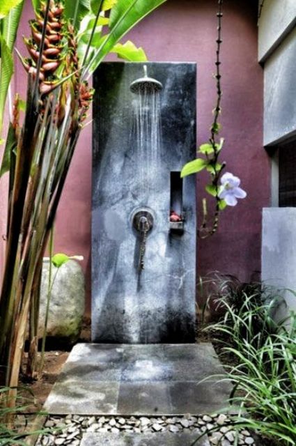 A tropical inspired outdoor shower with tropical plants and flowers and a concrete and plaster shower space
