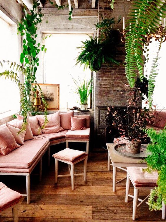a neutral sunroom filled wiht a lot of potted greenery and with a corner bench in dusty rose