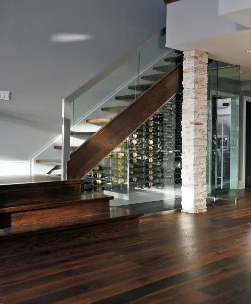 a whole wine room under the stairs with glass walls and lights inside looks very inviting