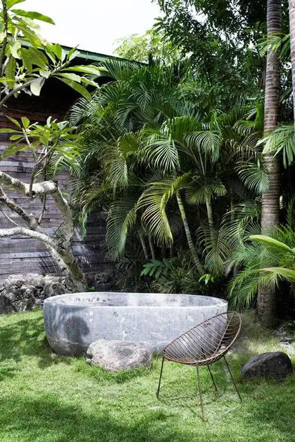 a gorgeous tropical outdoor space with only a stone carved bathtub and a metal chair, who needs more