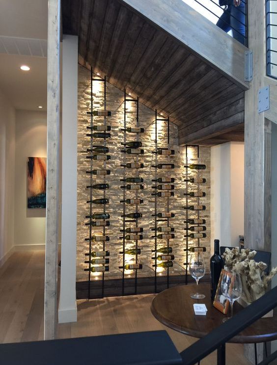an elegant wine cellar under the stairs with a stone clad wall and metal shelves that are lit up
