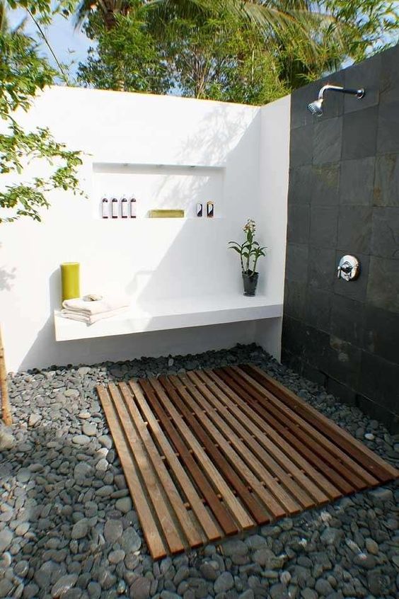 a contemporary outdoor shower of white concrete, tiles, pebbles on the floor and a wooden deck