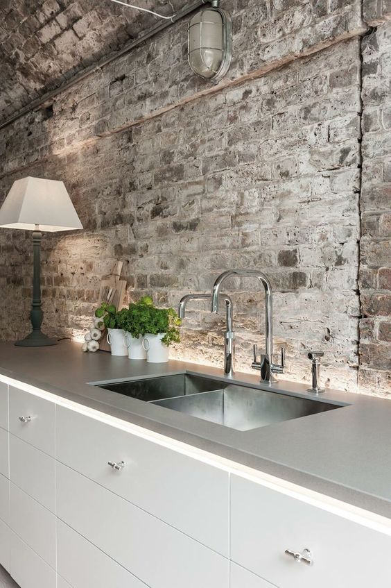 a contemporary industrial kitchen with rough grey brick walls and a ceiling plus stainless steel