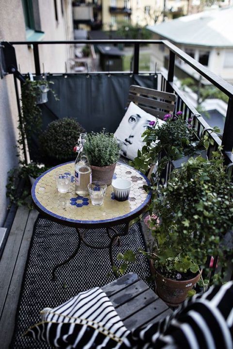 a monochromatic balcony with chairs and a lot of potted greenery is spruced up with a colorful mosaiic table