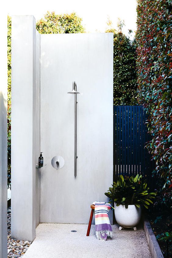a modern white concrete shower with a small wooden stool and a potted plant for a lively feel